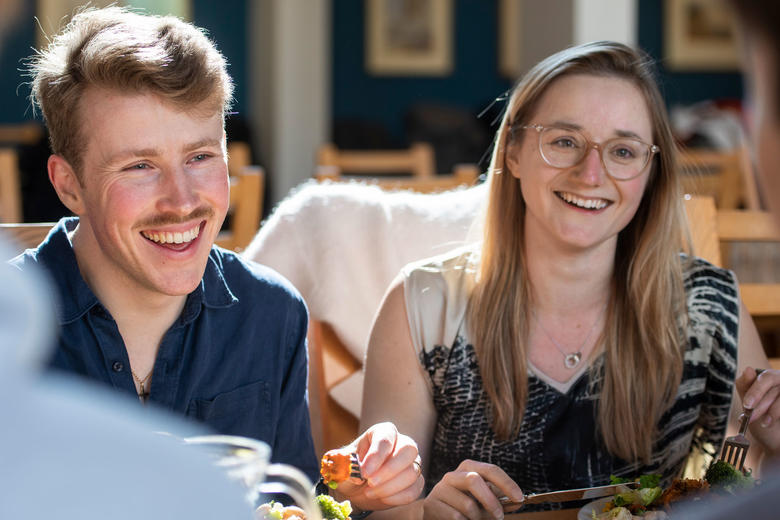 Two St Cross students one male, one female enjoying a meal in the dining hall
