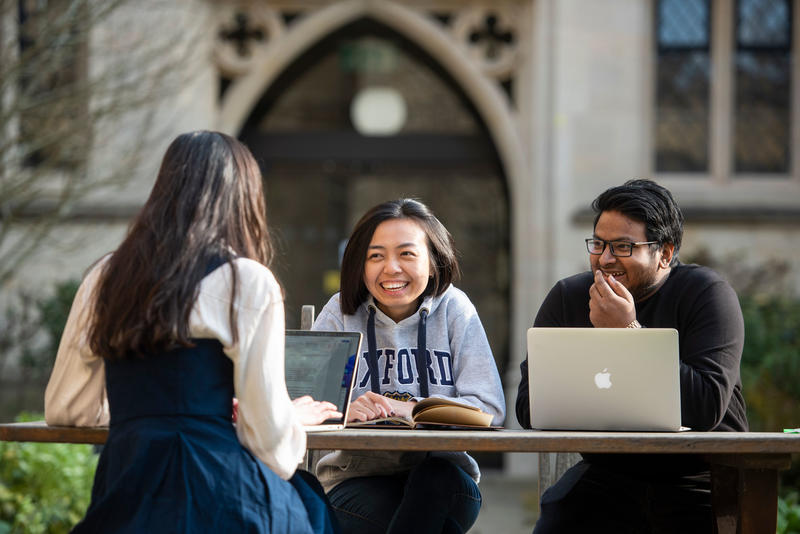 Three St Cross Students chatting at a bench in the quad